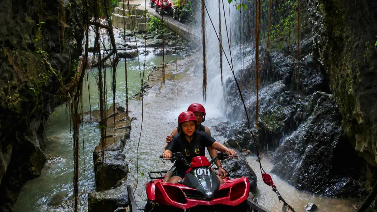 Quad bike crossing a river beside a waterfall on the Barong Caves ATV tour in Ubud, Bali